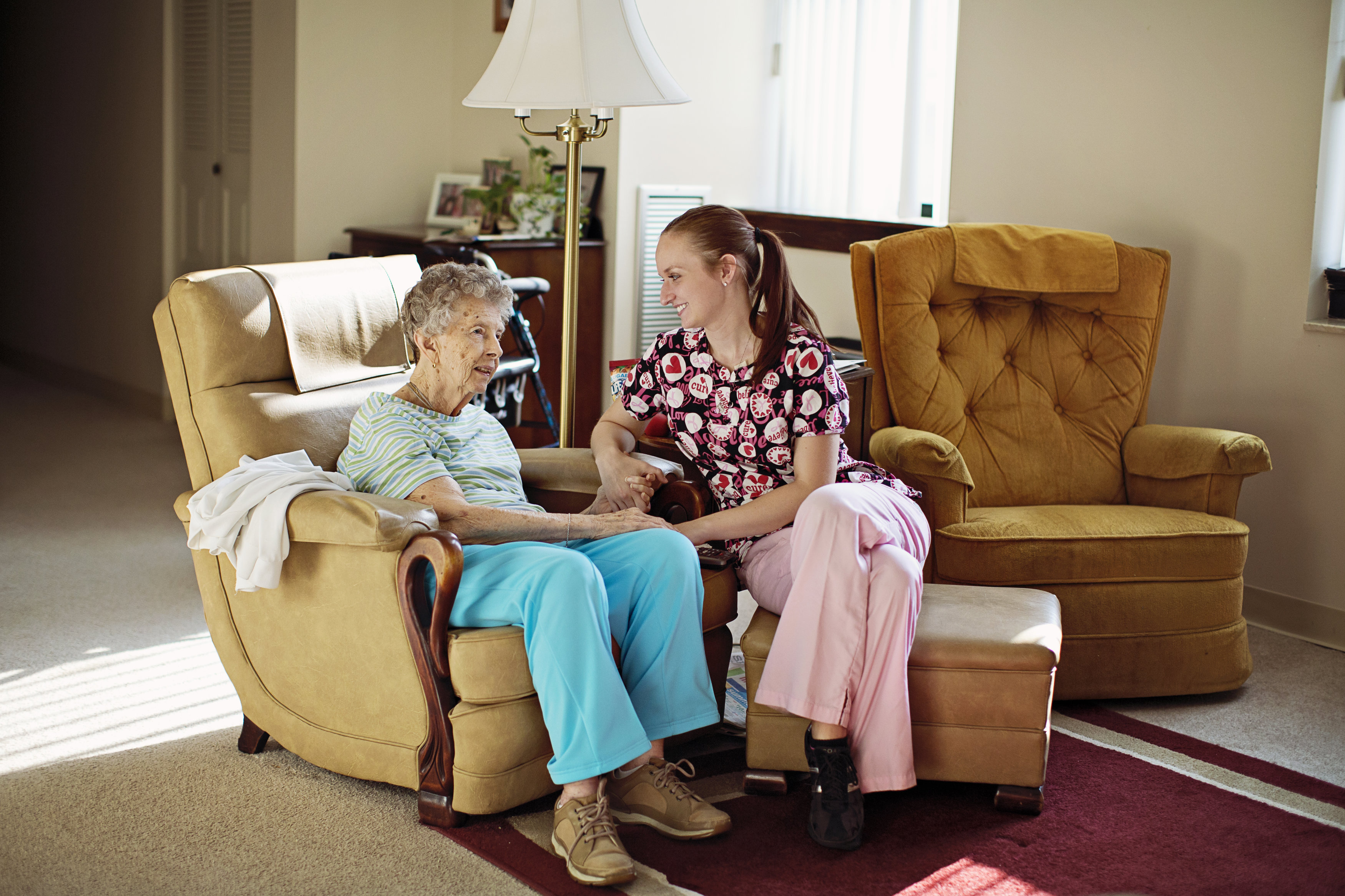 Home Health Caregiver sitting & holding hands of elderly companion care patient.
