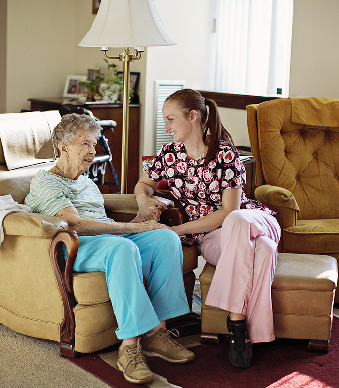Home Health Caregive sitting & holding hands of elderly companion care patient.